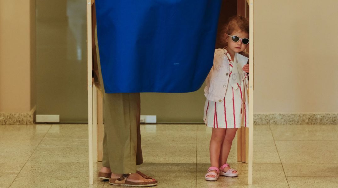 Ένα κοριτσάκι φαίνεται στην άκρη του παραβάν την ώρα που η μητέρα της ψηφίζει