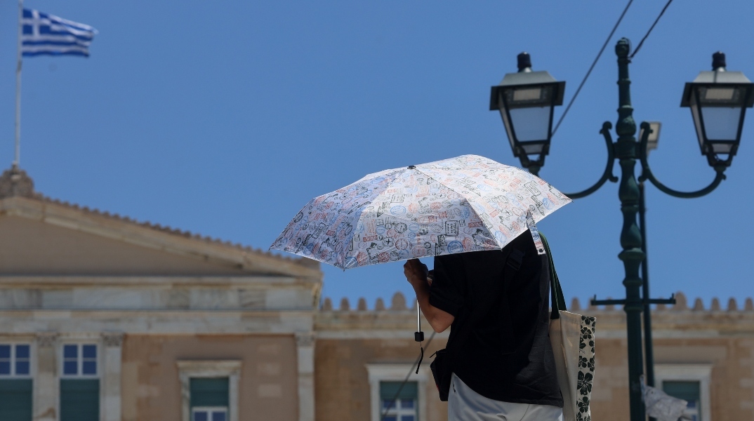 αθηναιος με ομπρελα μπροστα στη Βουλη, ελληνικη σημαια