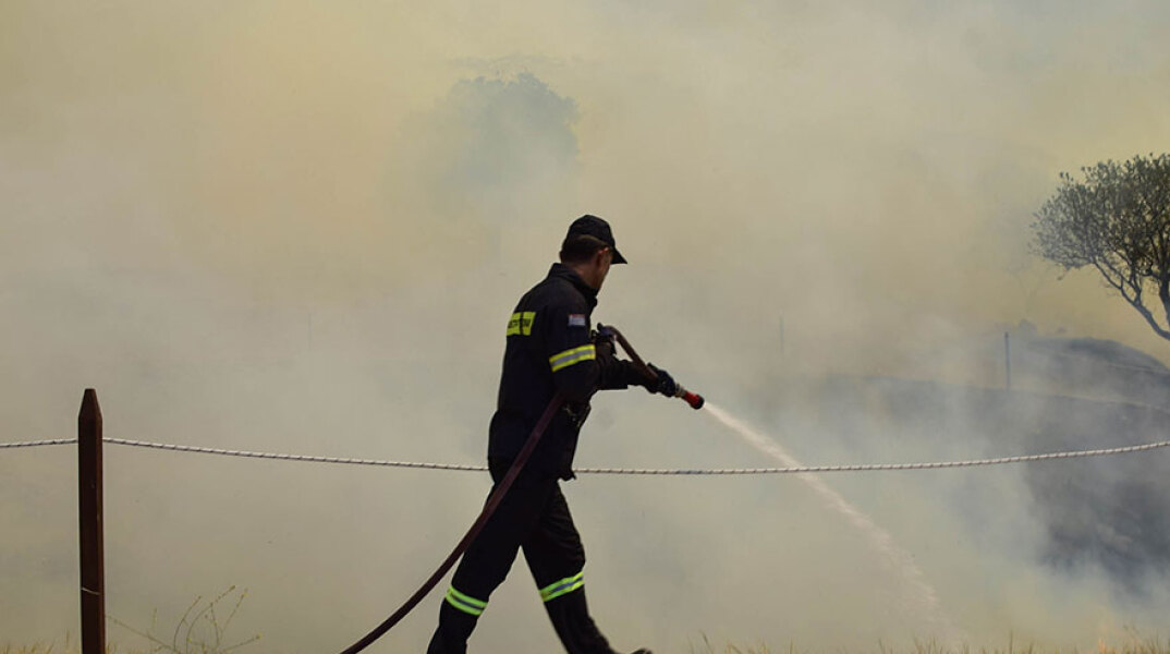 Πυροσβέστης ρίχνει νερό σε εστία πυρκαγιάς (ΦΩΤΟ ΑΡΧΕΙΟΥ) - Στα Καλύβια Αττικής εκδηλώθηκε φωτιά, προκαλώντας συναγερμό στην Πυροσβεστική Υπηρεσία