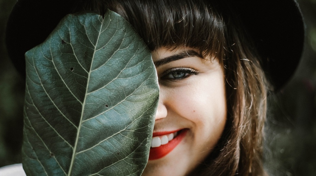 Γυναίκα που χαμογελά κρύβοντας το πρόσωπό της με πράσινο φύλλο