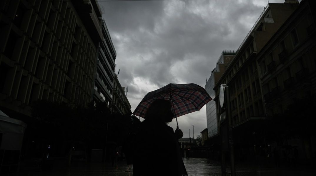 Πολίτης κρατά ομπρέλα για να προστατευτεί από τη βροχή σε σκοτεινιασμένο ουρανό