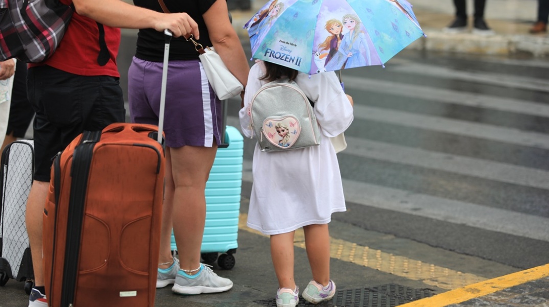 Παιδάκι κρατά ομπρέλα εν μέσω βροχής και περιμένει κοντά σε διάβαση πεζών