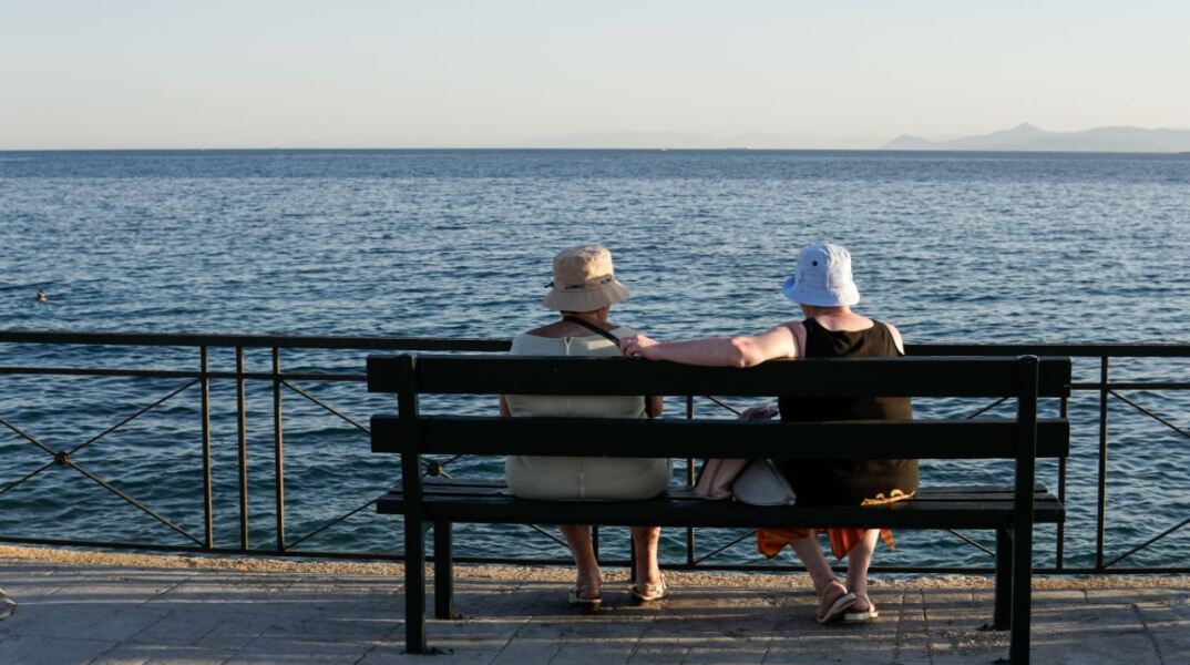 Ηλικιωμένοι κάθονται σε παγκάκι μπροστά στη θαλάσσα
