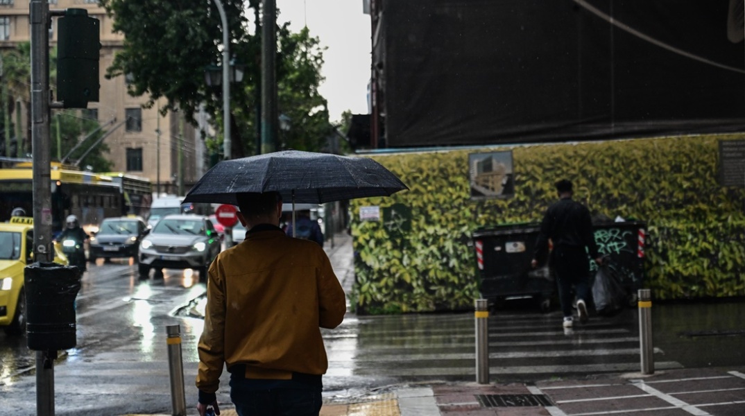 Άτομο με ομπρέλα προστατεύεται από μπόρα στο κέντρο της Αθήνας