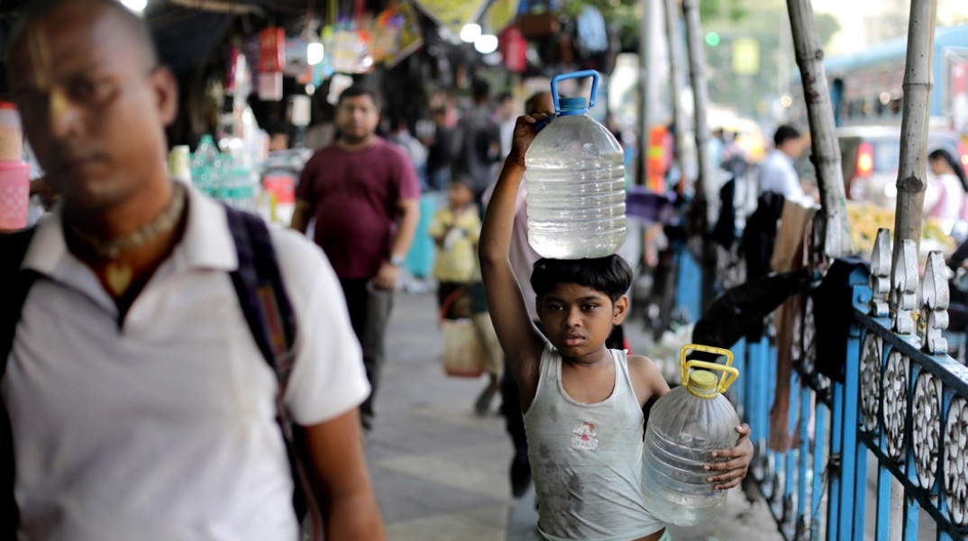 Παιδί στην Ινδία μεταφέρει μποτίλιες με νερό στο χέρι και στο κεφάλι του