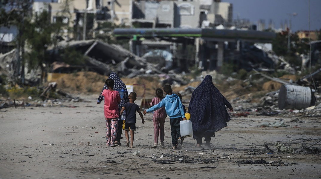 Παιδιά περπατούν δίπλα από βομβαρδισμένα κτίρια στη Γάζα