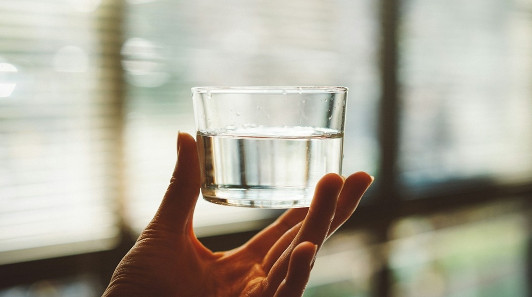 Χέρι κρατά μικρό ποτήρι με νερό ψηλά ώστε να διακρίνεται η διαύγεια του