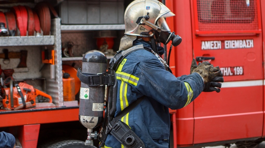 Πυροσβέστης με μαύρα από τον καπνό γάντια μπροστά από πυροσβεστικό όχημα