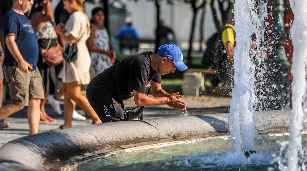 Πολίτης δροσίζεται βουτώντας τα χέρια του στο νερό του σιντριβανιού στο Σύνταγμα
