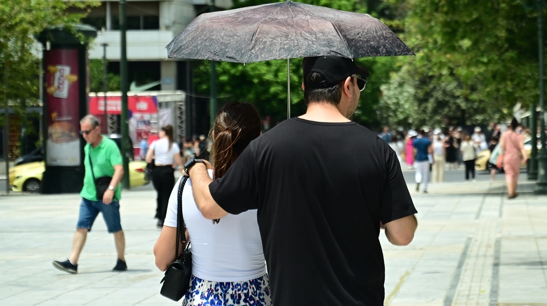 Ζευγάρι κρατά ομπρέλα για να προστατευτεί από τις ακτίνες του καυτού ήλιου