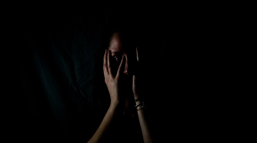 Γυναίκα που κλαίει κρατά το πρόσωπό της ενώ βρίσκεται στο ημίφως - Εικόνα που παραπέμπει σε κακοποίηση και ενδοοικογενειακή βία