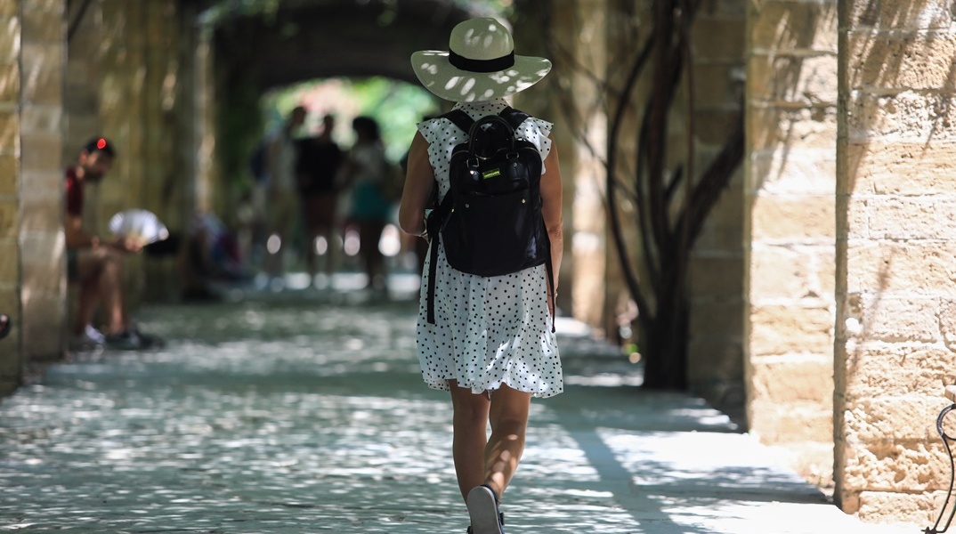 Γυναίκα με καπέλο και καλοκαιρινά ρούχα περπατά στον Εθνικό Κήπο