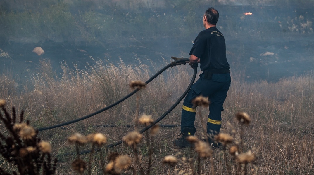 Πυροσβέστης με τη μάνικα επιχειρεί για την κατάσβεση φωτιάς σε χαμηλή βλάστηση