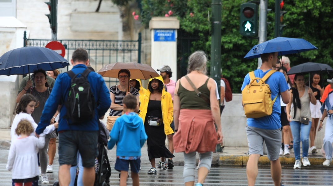 Πολίτες στο κέντρο της Αθήνας κρατούν ομπρέλα για να προστατευτούν από τη βροχή