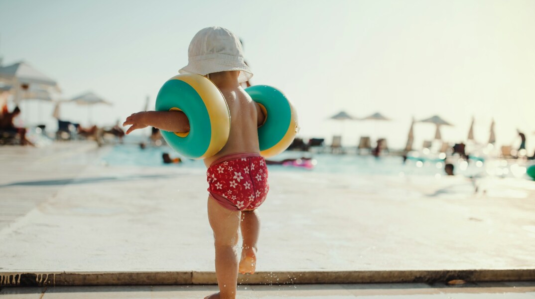 Παιδάκι με μπρατσάκια σε εξέδρα οργανωμένης παραλίας έχει την πλάτη στον φακό