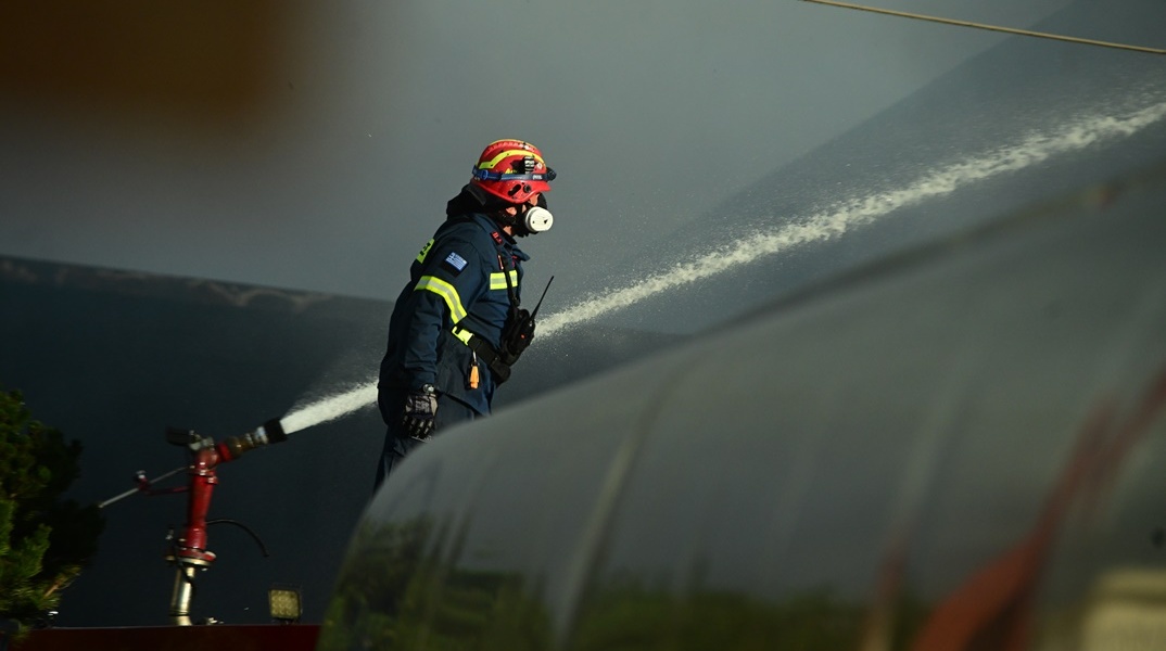 Πυροσβέστης δίπλα από μάνικα που ρίχνει νερό για την κατάσβεση φωτιάς