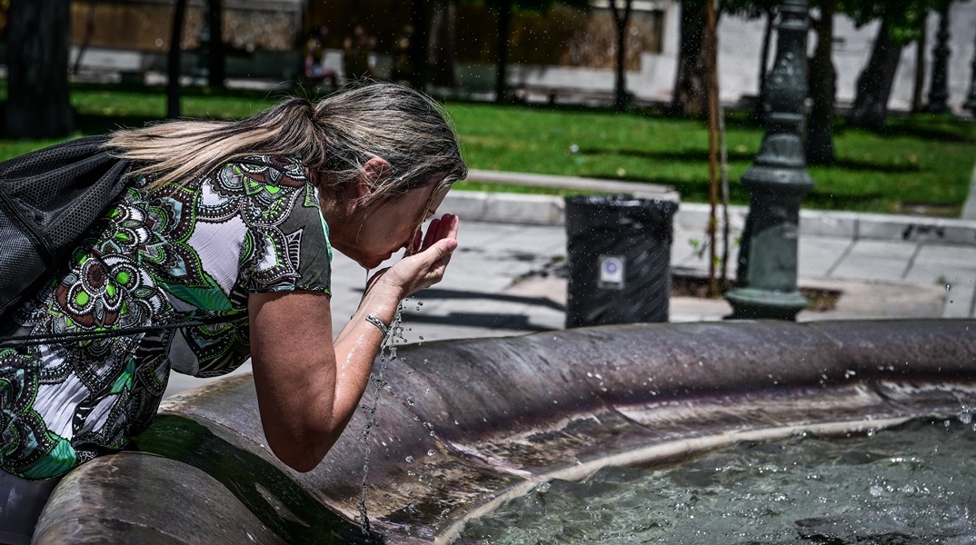 Γυναίκα δροσίζεται ρίχνοντας νερό στο πρόσωπό της από το σιντριβάνι στο Σύνταγμα