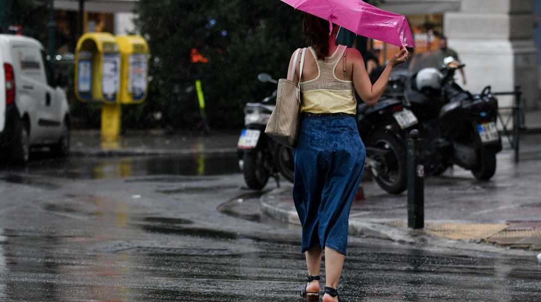 Κοπέλα κρατά ομπρέλα για να μην βραχεί από καλοκαιρινό μπουρίνι