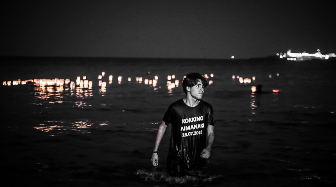 Νεαρό άτομο βγαίνει από τη θάλασσα όπου έχει αφήσει το φαναράκι του με μπλουζάκι που γράφει «Κόκκινο Λιμανάκι 23.07.2018»