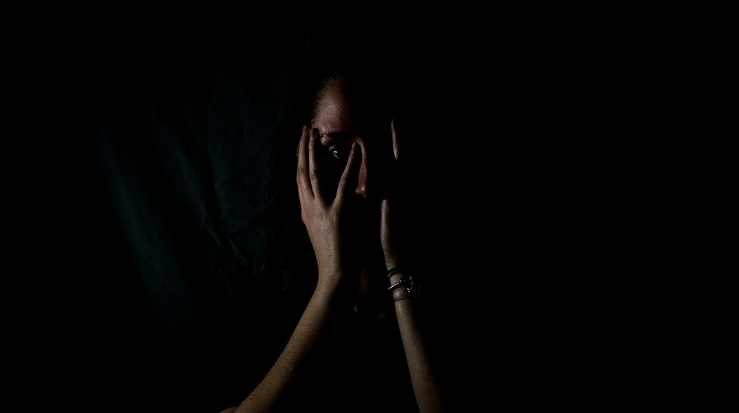 Γυναίκα σε σκοτεινό δωμάτιο κρατά το κεφάλι της
