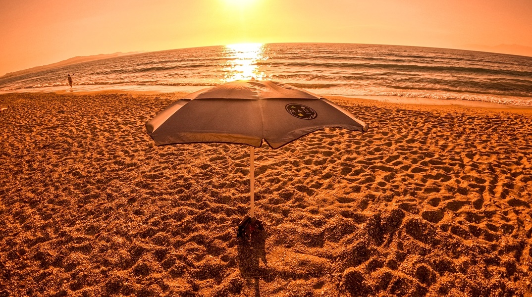 Φωτογραφία από παραλία εν μέσω καύσωνα με τον φακό να καταγράφει τον ήλιο και ομπρέλα σε παραλία