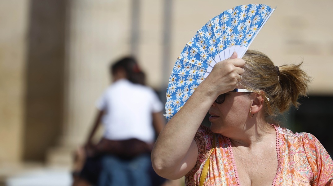 Γυναίκα κρατά στο κεφάλι της την βεντάλια της για να προφυλαχτεί από τον ήλιο