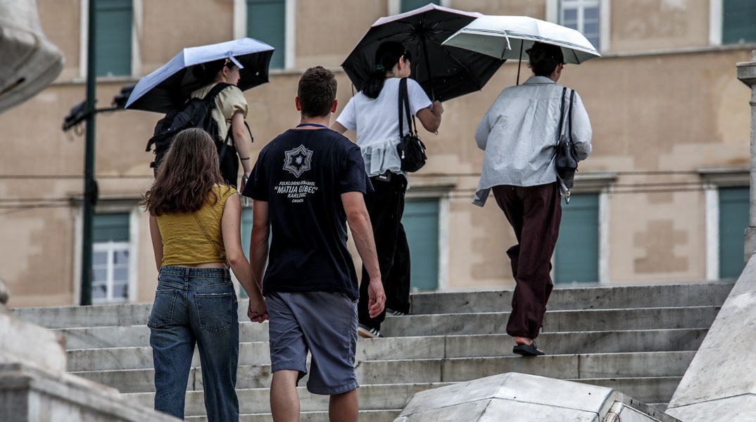 Πολίτες, άλλοι με ομπρέλες και άλλοι χωρίς, ανεβαίνουν τα σκαλάκια της πλατείας Συντάγματος