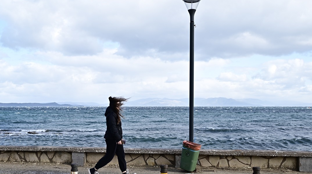 Κρύο και δυνατοί άνεμοι - Γυναίκα που περπατά υπό αυτές τις συνθήκες δίπλα στη θάλασσα