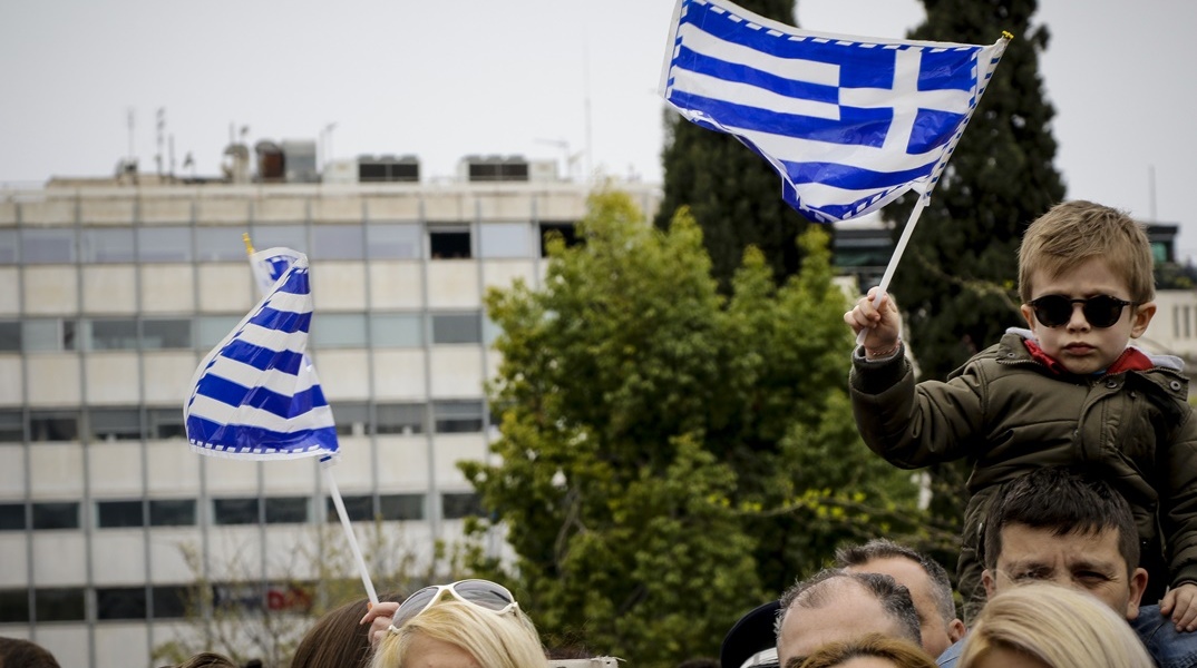 Παιδάκι στους ώμους του μπαμπά του κρατά την ελληνική σημαία