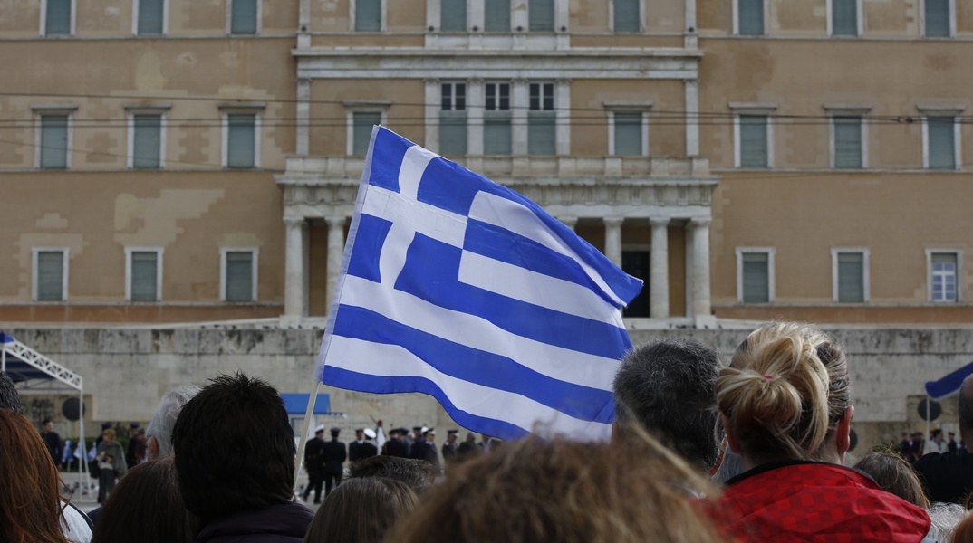 Πολίτες κρατούν ελληνική σημαία μπροστά από τη Βουλή