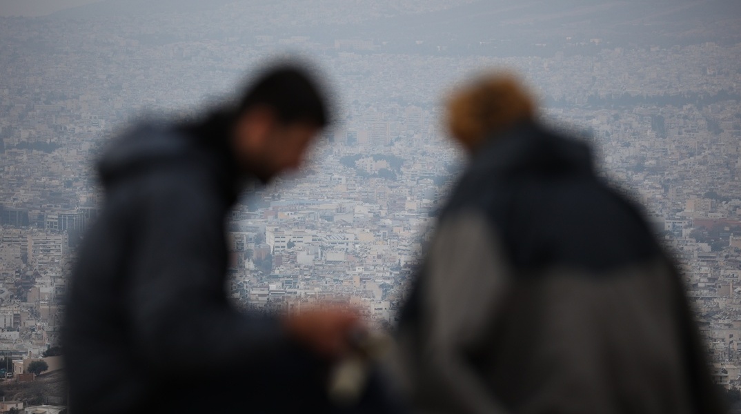 Δύο άτομο με φόντο τη συννεφιασμένη Αθήνα