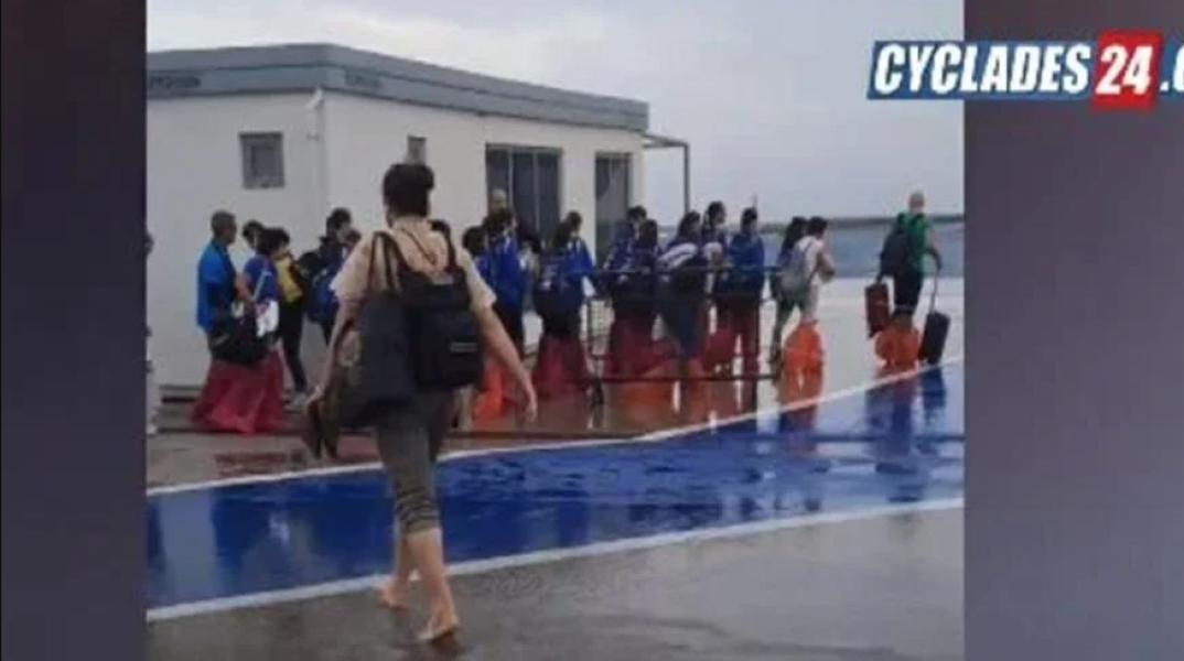 Επιβάτες μπαίνουν στο πλοίο στο λιμάνι της Τήνου ξυπόλητοι ή με σακούλες στα πόδια λόγω των κυμάτων
